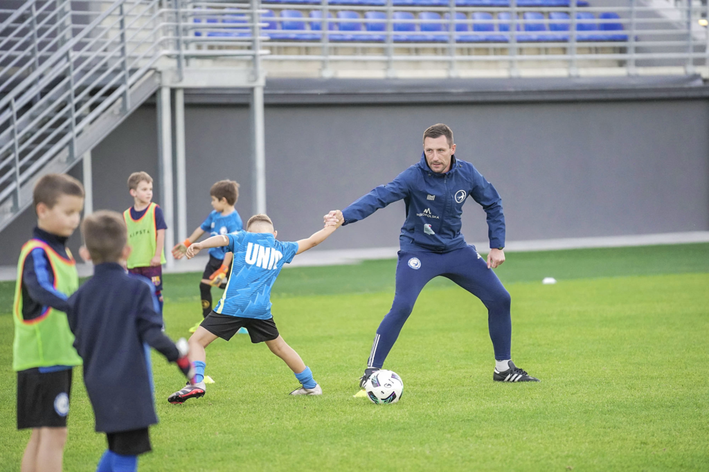 Trener prowadzi ćwiczenie z piłką z młodymi zawodnikami Akademii.